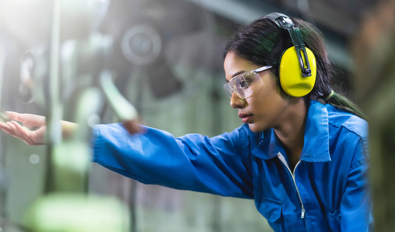 A worker in protective eyewear and ear defenders operating equipment